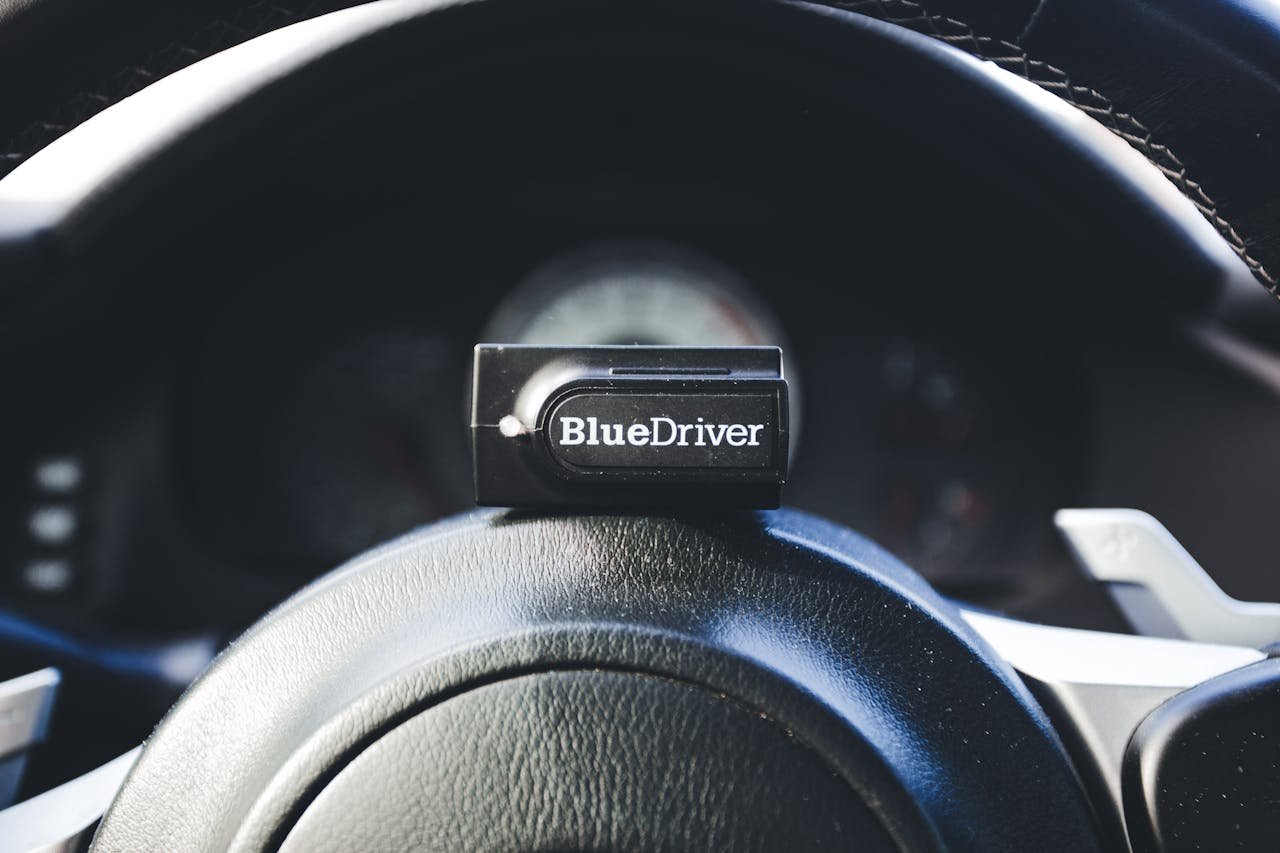A BlueDriver code reader placed on a cars steering wheel, showcasing automotive diagnostic tools.